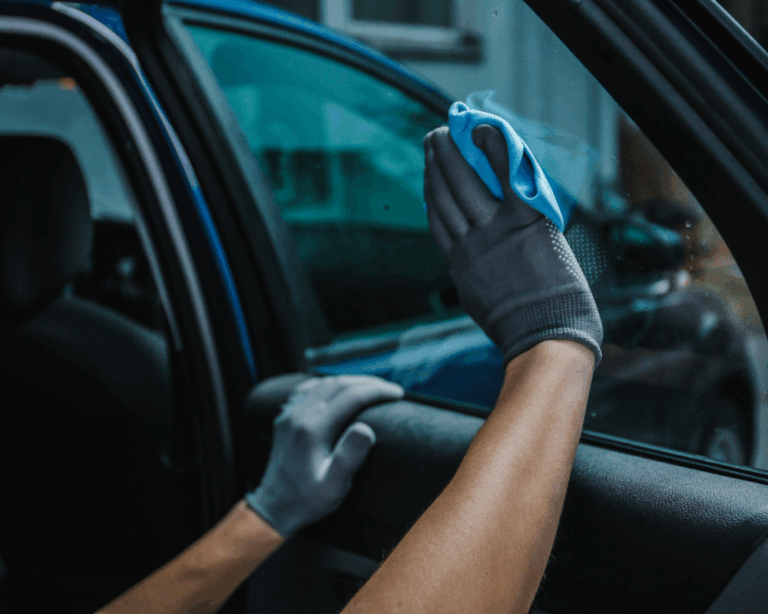 A person in gray gloves cleans the inside of a car window with a blue cloth, focusing on clarity and shine.