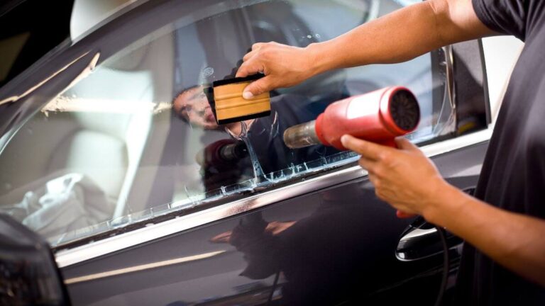 A person applying window tint to a car using a heat gun and a squeegee.