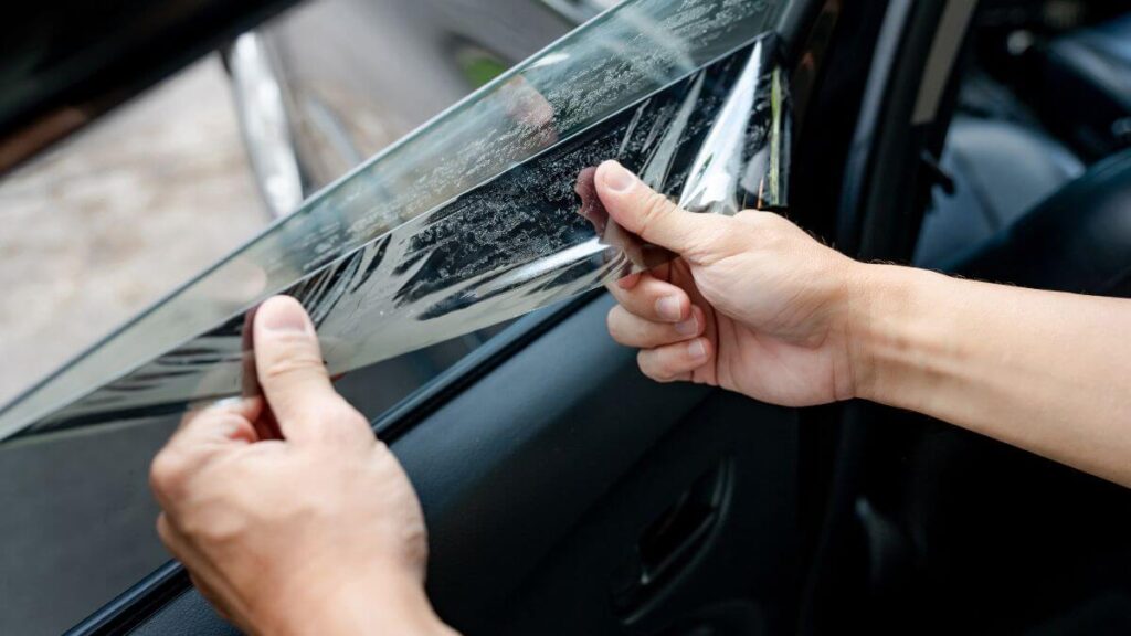A person is removing a window film from a car window.